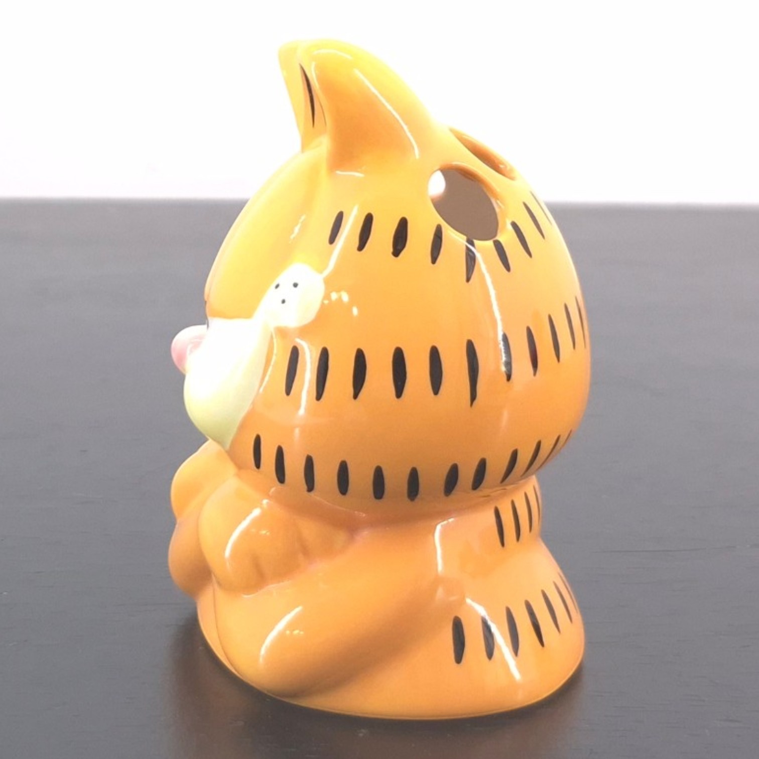 Garfield Toothbrush Holder _left - Orange ceramic tiger figurine with black stripes, viewed from the side on a dark surface.