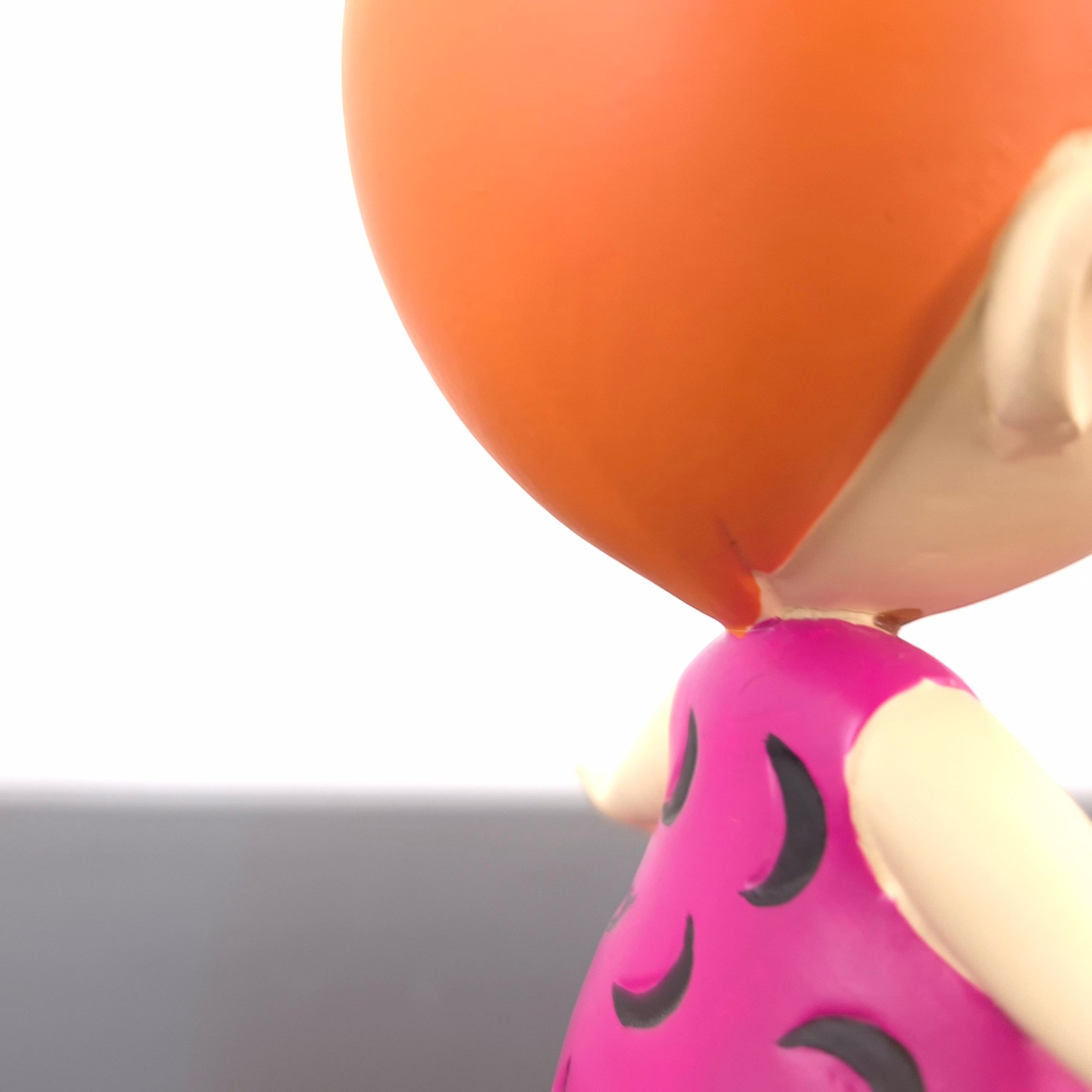Pebbles Flintstones Jewellery Holder _detail right - Close-up of a colorful balloon figure: orange head and bright pink outfit with black crescent patterns against a white background.